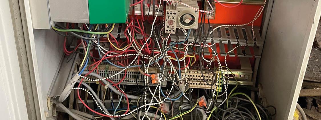 Open industrial electrical cabinet with dense wiring, terminal blocks, relays, and control components.